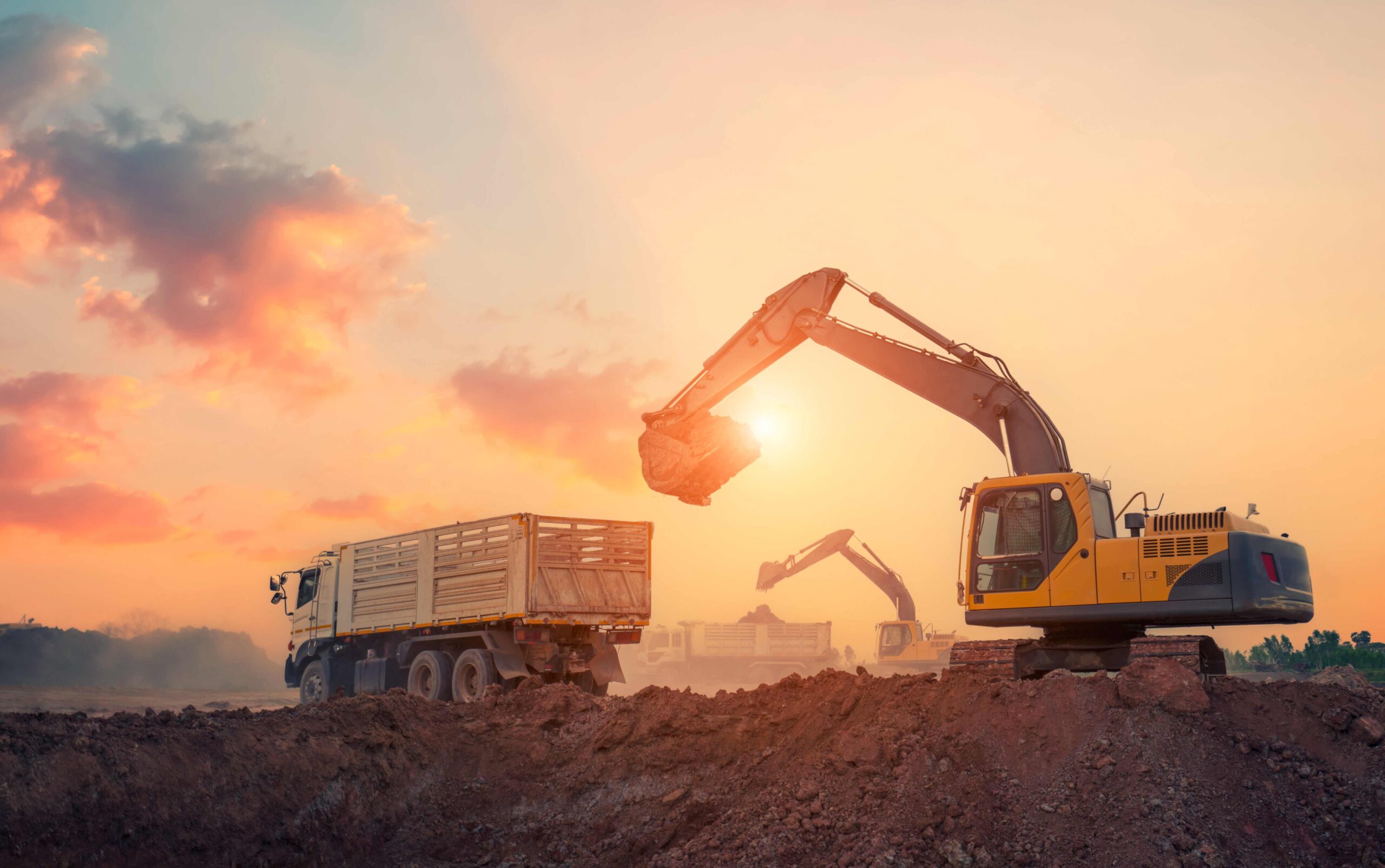 Crawler excavators during heavy earthwork on construction site at sunset moving rubble